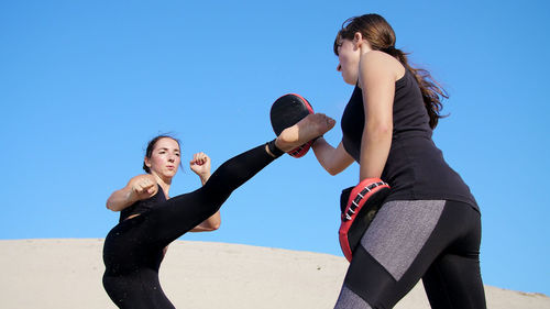 Two athletic, young women in black fitness suits are engaged in a pair work out kicks train to fight