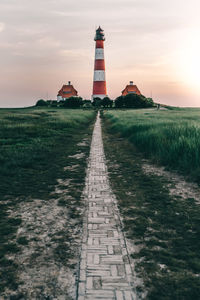 Lighthouse on field by building against sky during sunset