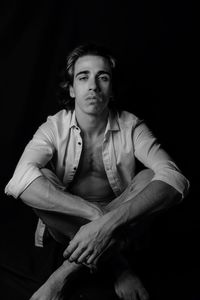 Portrait of young man sitting against black background