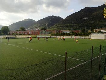 People playing soccer field against sky