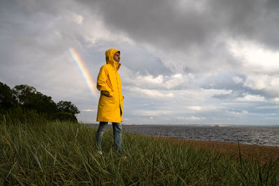 Man in yellow raincoat with hood walk on the beach in rainy weather