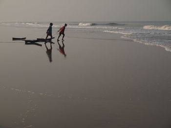 People walking at beach against sky during sunset