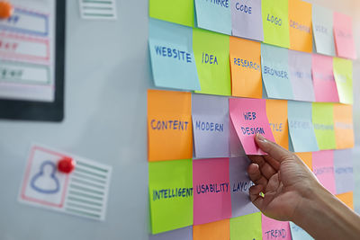 Cropped hand of businesswoman holding sticking note stuck on wall