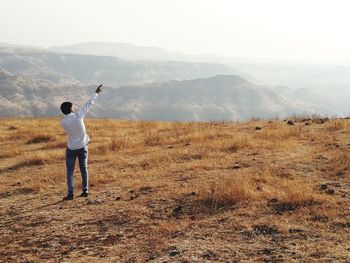 Rear view of man standing on field against mountain