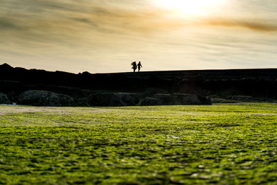 Silhouette man standing on field against sky during sunset