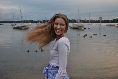 Side view portrait of cheerful young woman tossing hair while standing by sea