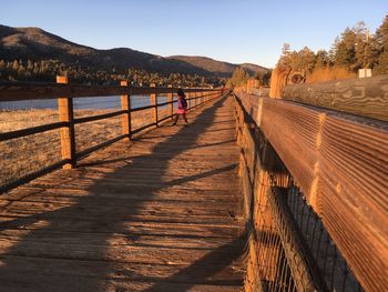 Girl walking on footbridge against clear sky