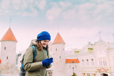 Smiling woman using mobile phone standing against buildings