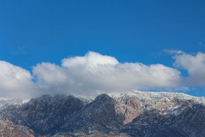 Low angle view of snowcapped mountains against blue sky