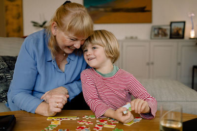 Smiling grandson and grandmother playing with jigsaw puzzle at home