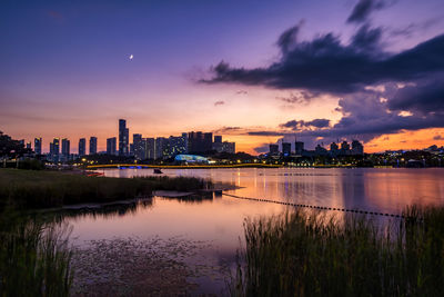 Scenic view of the lake by buildings against the sky at sunset