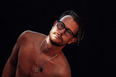 Portrait of shirtless young man against black background