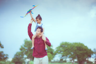 Father carrying daughter on shoulder against sky