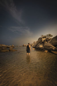 Man standing on rock at beach against sky