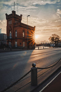 Road by building against sky during sunset in city