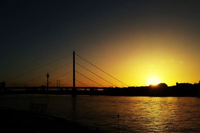 Silhouette bridge over river against sky during sunset
