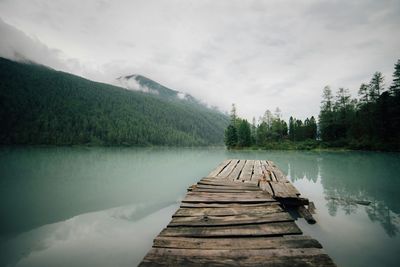 Pier on lake against cloudy sky