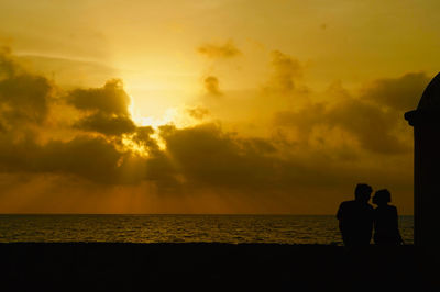 Silhouette couple on beach against orange sky