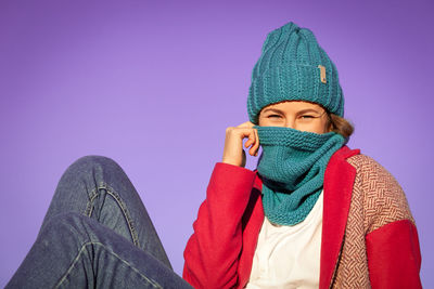 Portrait of a beautiful young model in knitted hat and warm clothes mysteriously holds a scarf 