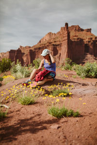 Woman hiker adjust her hat while resting amongst yellow desert flowers