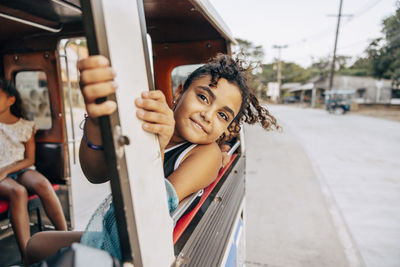 Smiling girl leaning out of window during road trip while sitting in tuk-tuk on vacation