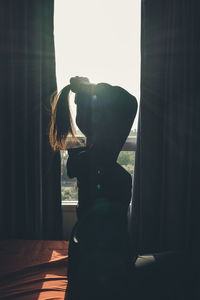 Young woman tying hair while sitting by window at home