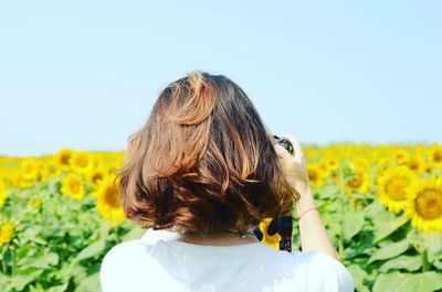 Rear view of woman in sunflower field against clear sky