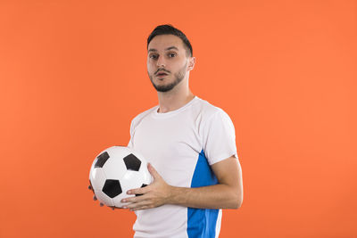 Portrait of young man holding soccer ball against yellow background