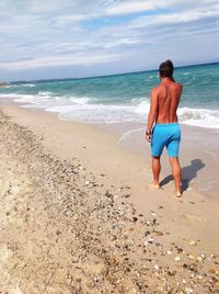 Rear view of shirtless man standing on beach against sky