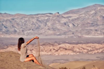 Side view of woman playing with sand dunes at desert