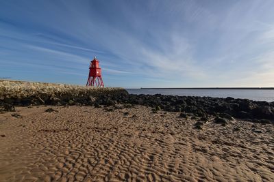 Lighthouse on beach against sky