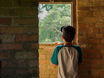 Rear view of boy standing against brick wall