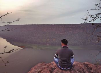 Nature theories- rear view of man sitting on rock against sky