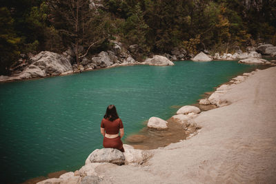 Rear view of man sitting on rock by lake