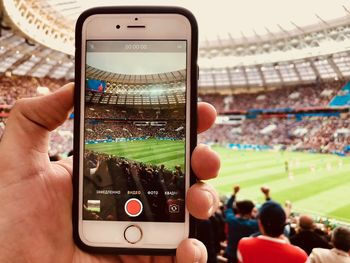 Cropped image of person photographing stadium through mobile phone