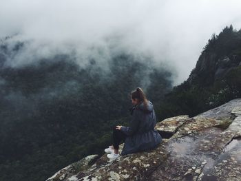 High angle view of young woman sitting on mountain during foggy weather