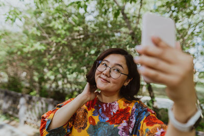 Smiling adult woman taking selfie outdoors with her smartphone