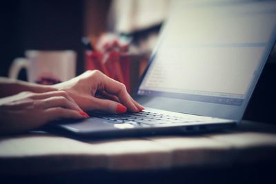 Cropped image of woman hands with red nail polish using laptop