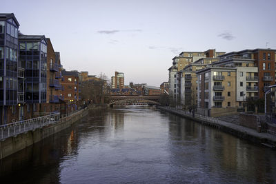 Canal amidst buildings in city against sky at dusk