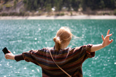 Rear view of woman with arms raised standing in sea