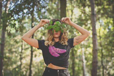 Mid adult woman covering eyes with leaves at forest