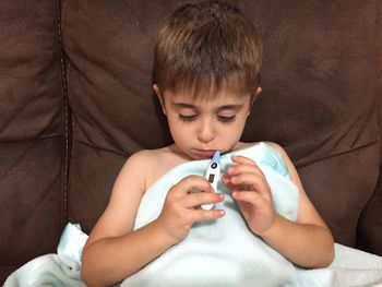 Boy using thermometer on sofa at home