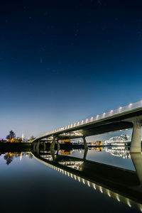 Low angle view of illuminated bridge over river against sky at night