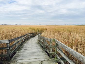 Boardwalk on field against sky