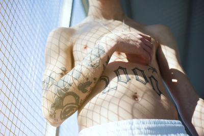 Midsection of shirtless young man with tattoo standing indoors