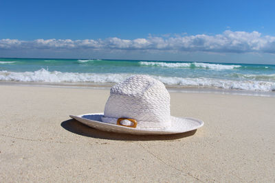 Close-up of white sun hat on shore at beach against sky