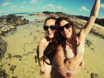 Smiling young women taking selfies at beach against sky