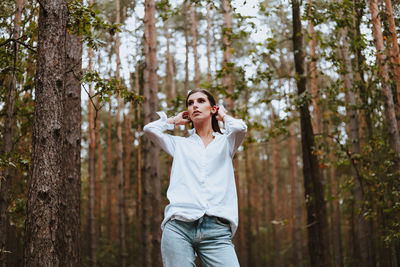 Young woman standing against trees in forest