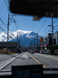 Cars on road by railroad tracks in city against sky