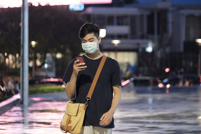 Young man wearing mask using phone standing on road